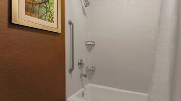 A bathroom with a white bathtub, a showerhead, and a handrail.