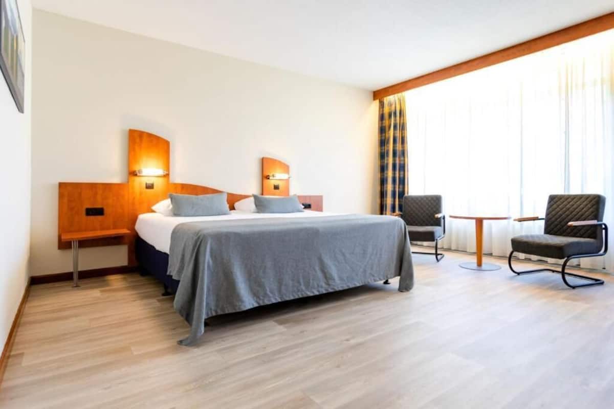 A hotel room with a bed, two bedside tables, a chair, and a small table.