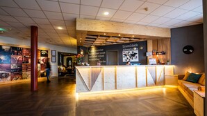 A reception area with a wooden reception desk, a large pillar, and a wall with travel-related posters. - Fletcher Hotel - Restaurant De Reiskoffer (Bosschenhoofd)