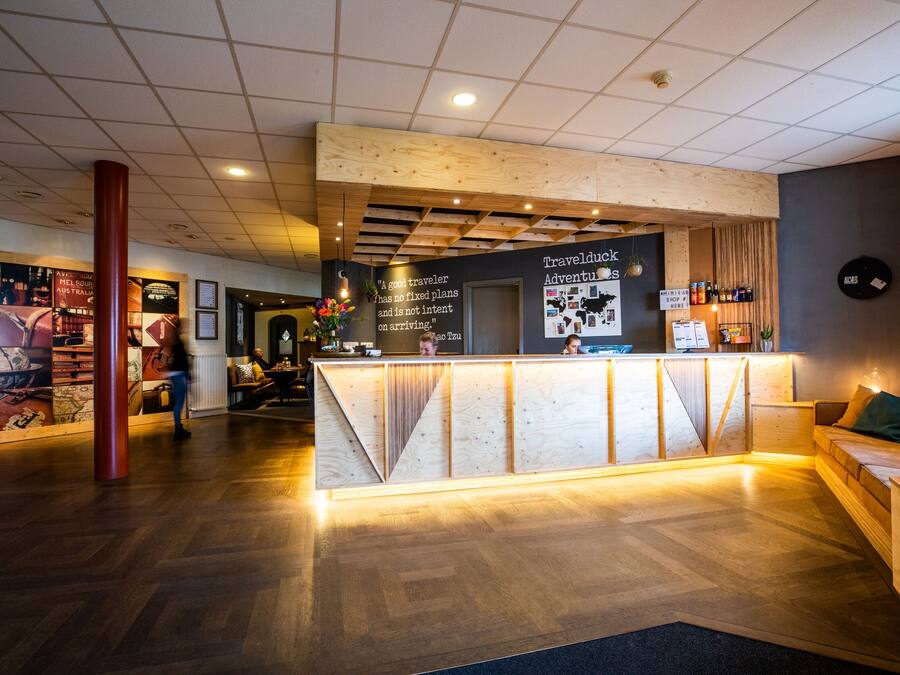 A reception area with a wooden reception desk, a large pillar, and a wall with travel-related posters.