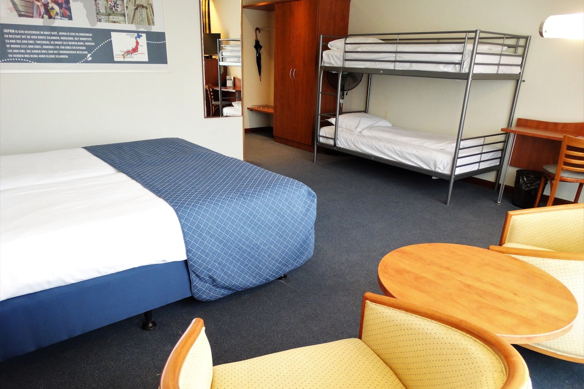 A hotel room with a bunk bed, a single bed, a small table, and a chair.