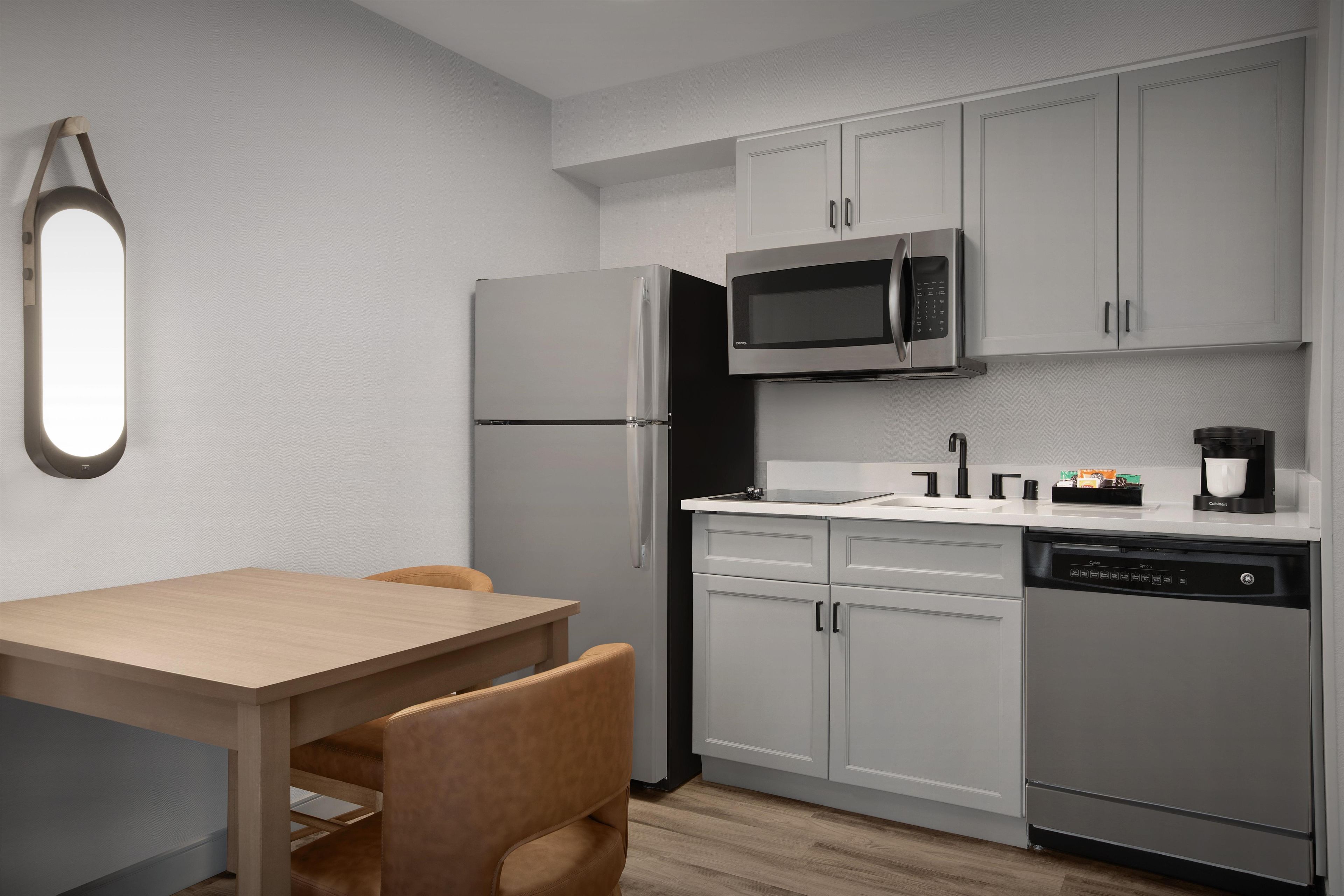 A modern kitchen with a refrigerator, microwave, dishwasher, and a dining area with a table and chairs.
