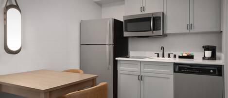A modern kitchen with a refrigerator, microwave, dishwasher, and a dining area with a table and chairs.