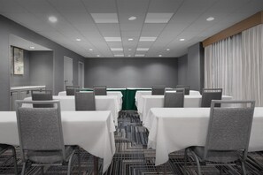 Un salón de conferencias con mesas y sillas, un camino de mesa verde y una alfombra estampada.