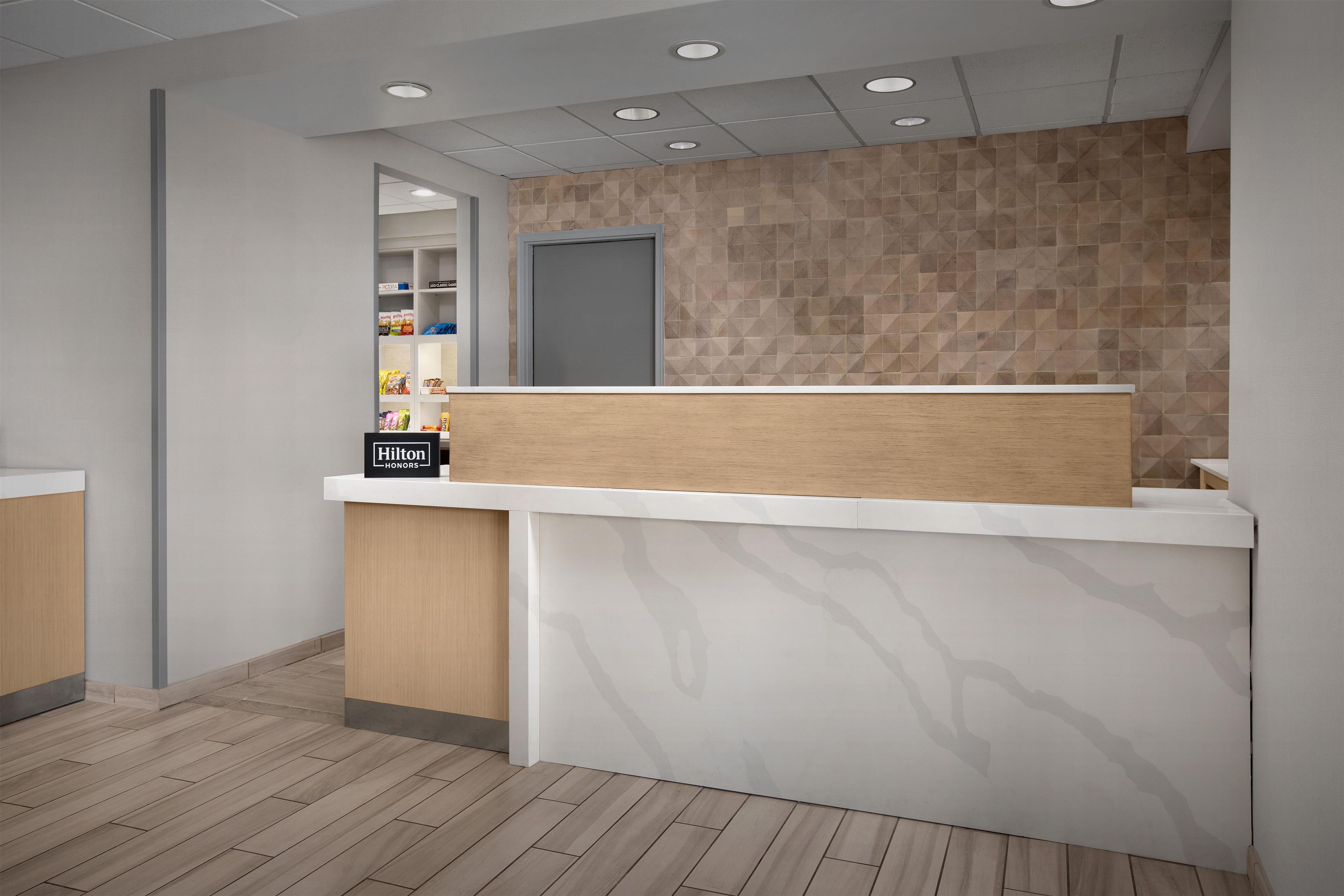 A hotel reception area with a wooden reception desk, a white counter, and a patterned wall.