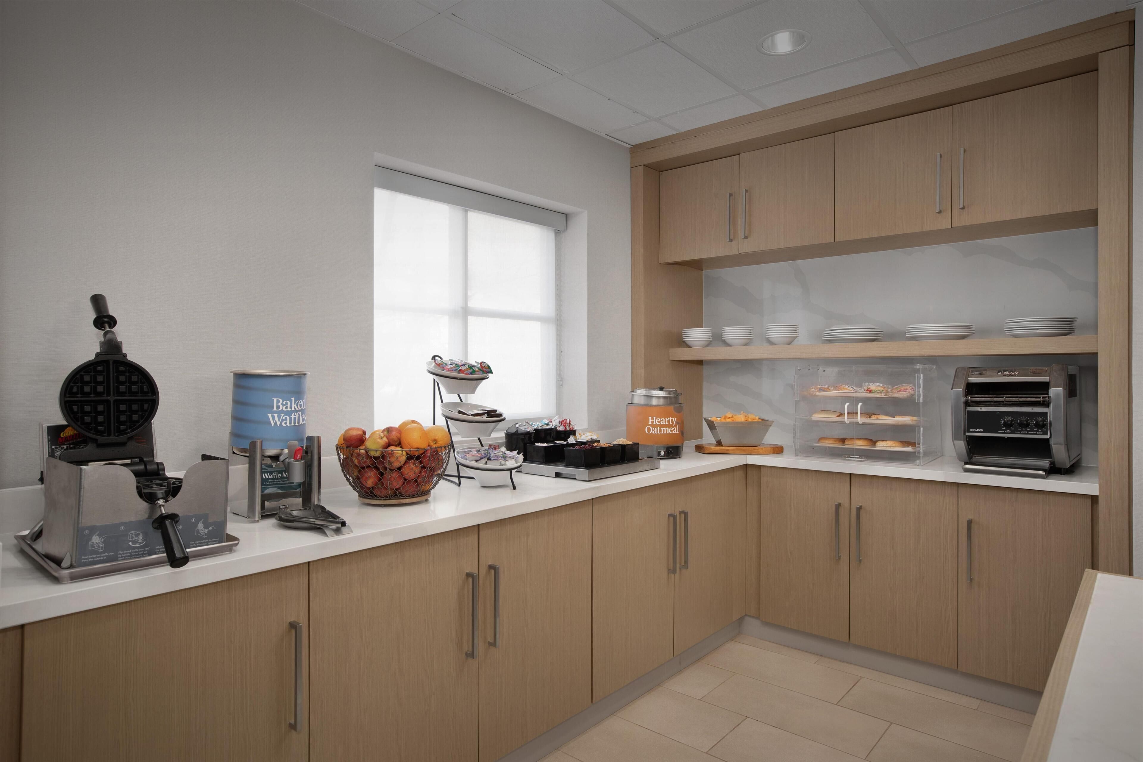 A modern kitchen with a waffle maker, waffle maker box, bowl of fruit, and a jar of oatmeal.