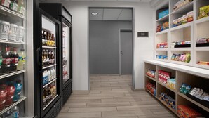 En hotellkorridor med en minibar, hyllor fyllda med snacks och drycker samt en skylt som visar vägen till hotellets butik.