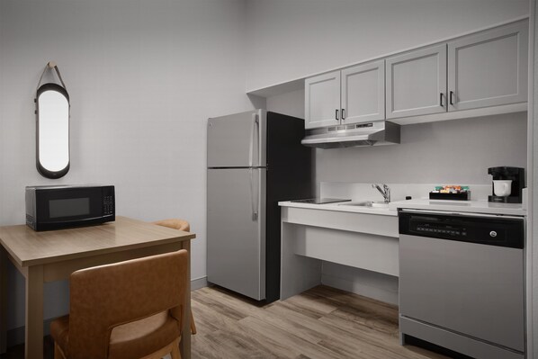 Una cocina moderna con microondas, refrigerador, lavavajillas y una mesa de madera con una silla.