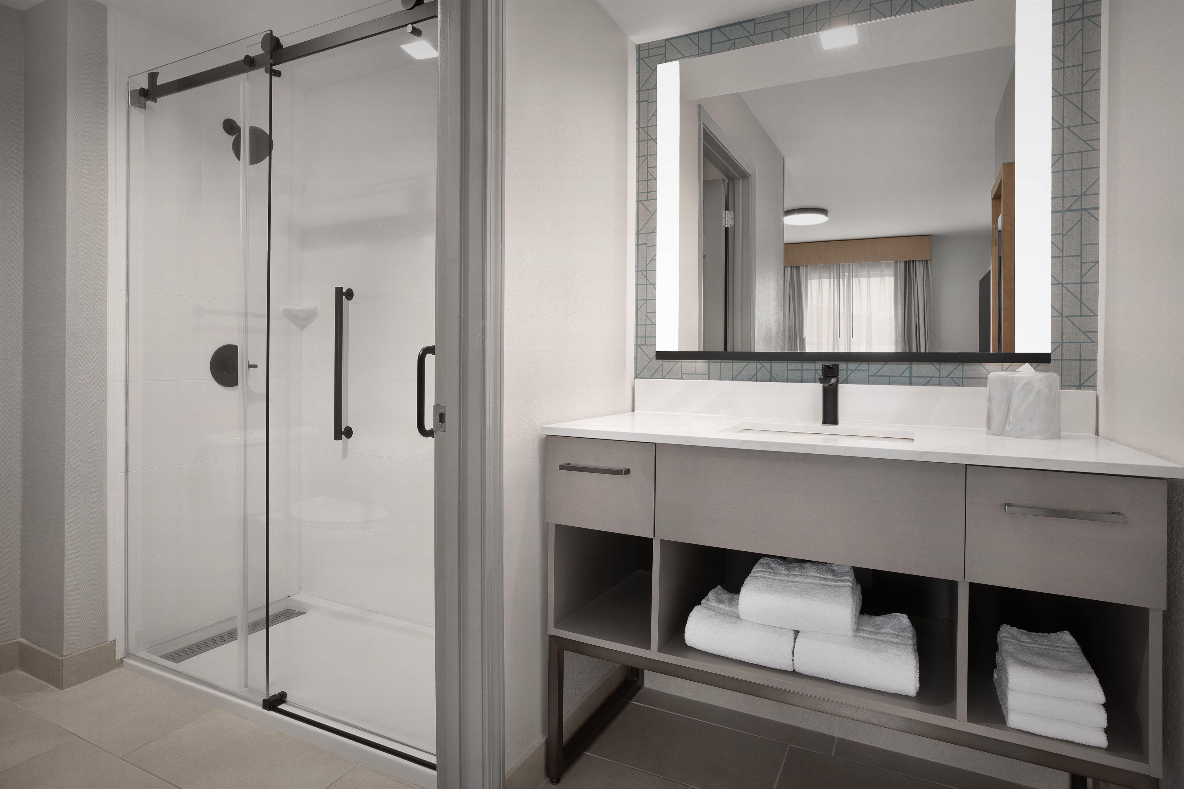 A modern bathroom with a glass-enclosed shower, a vanity with a mirror, and a towel rack.