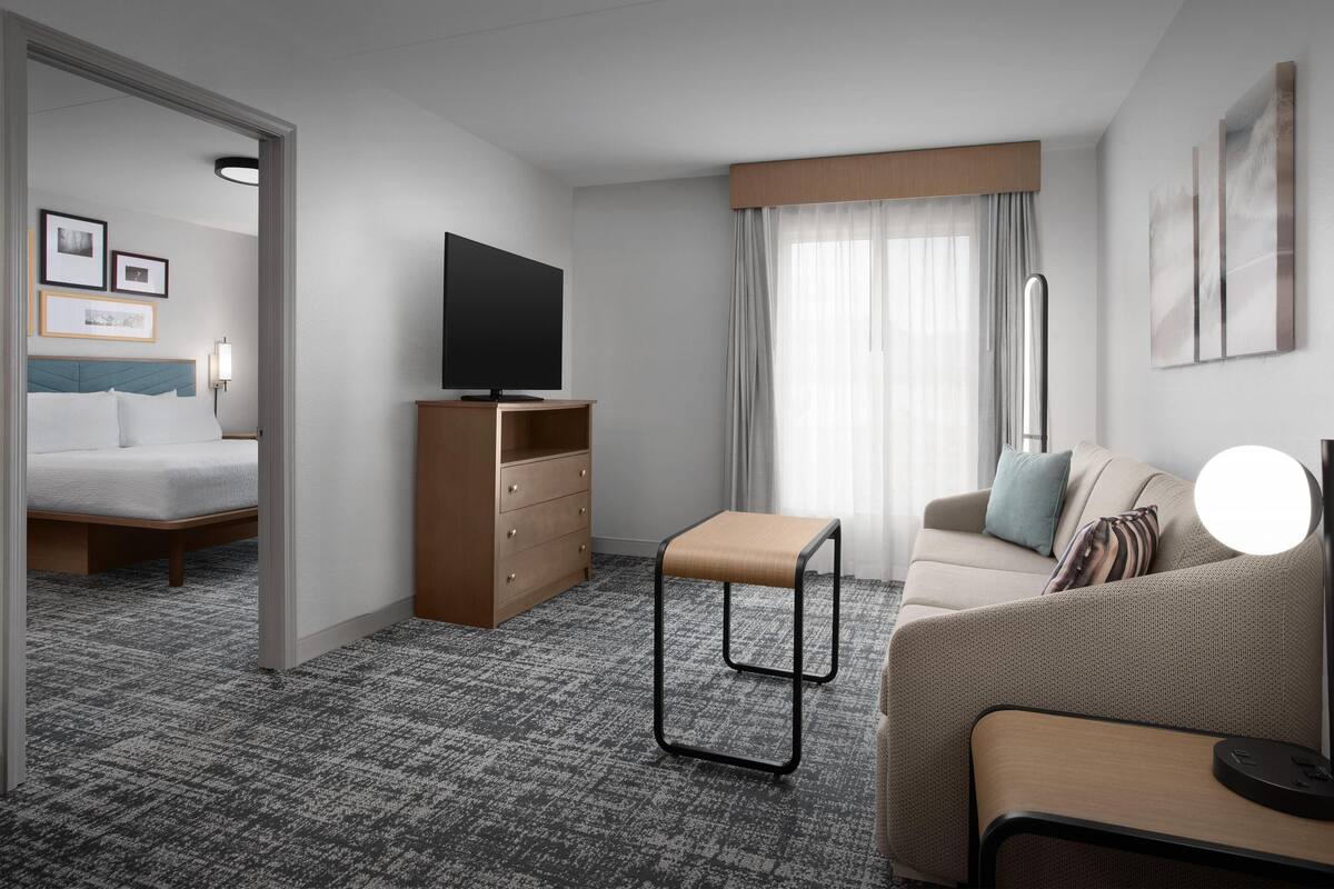 Una habitación de hotel con cama, televisor, sofá, una mesita y espejo.
