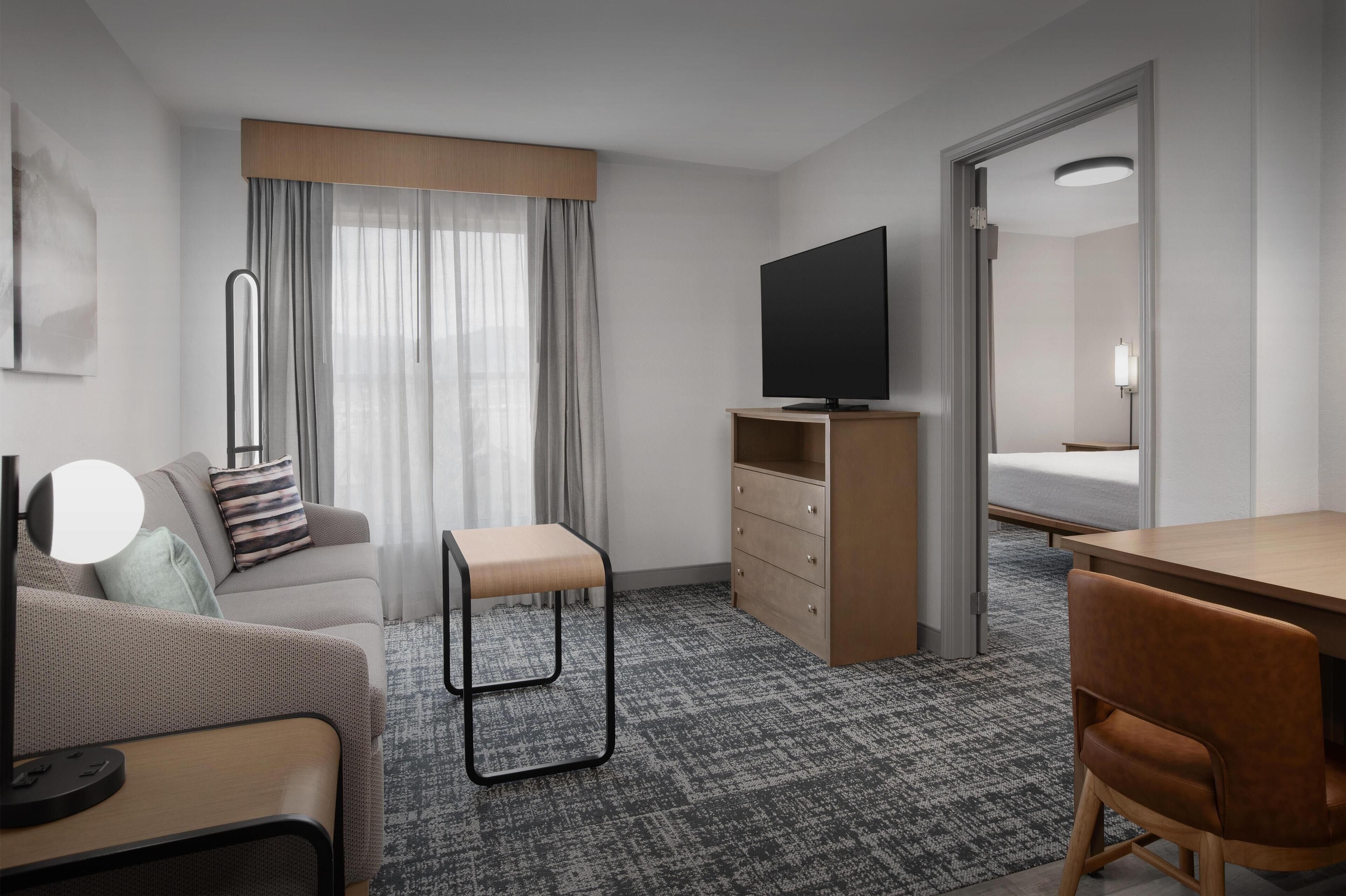 Une chambre d’hôtel avec un canapé, une petite table, une télévision, un bureau, une chaise, une armoire et un lit.