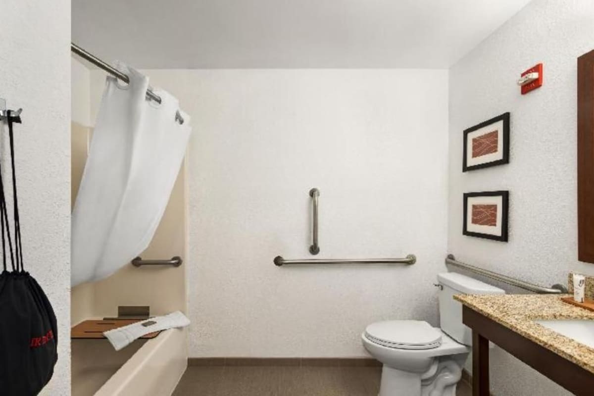 A small, clean bathroom with a toilet, a shower curtain, a grab bar, and a sink with a countertop.