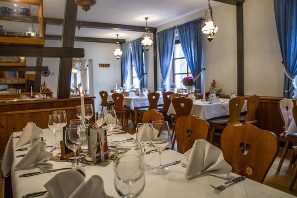 Un restaurant avec des chaises en bois, des nappes blanches et des luminaires suspendus.