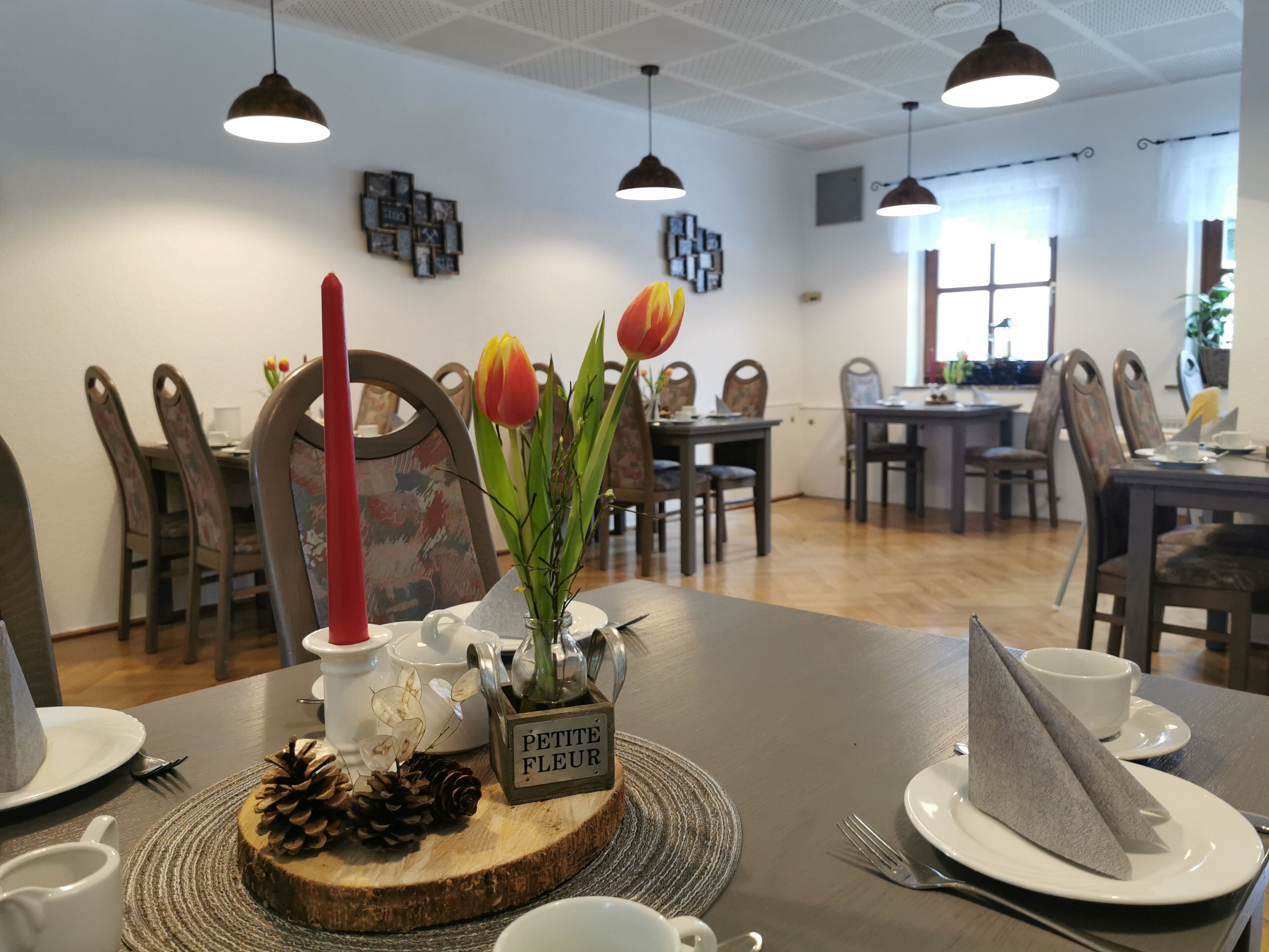 A dining area with a wooden table set for a meal, featuring a centerpiece with a vase of flowers, a pine cone, and a candle.