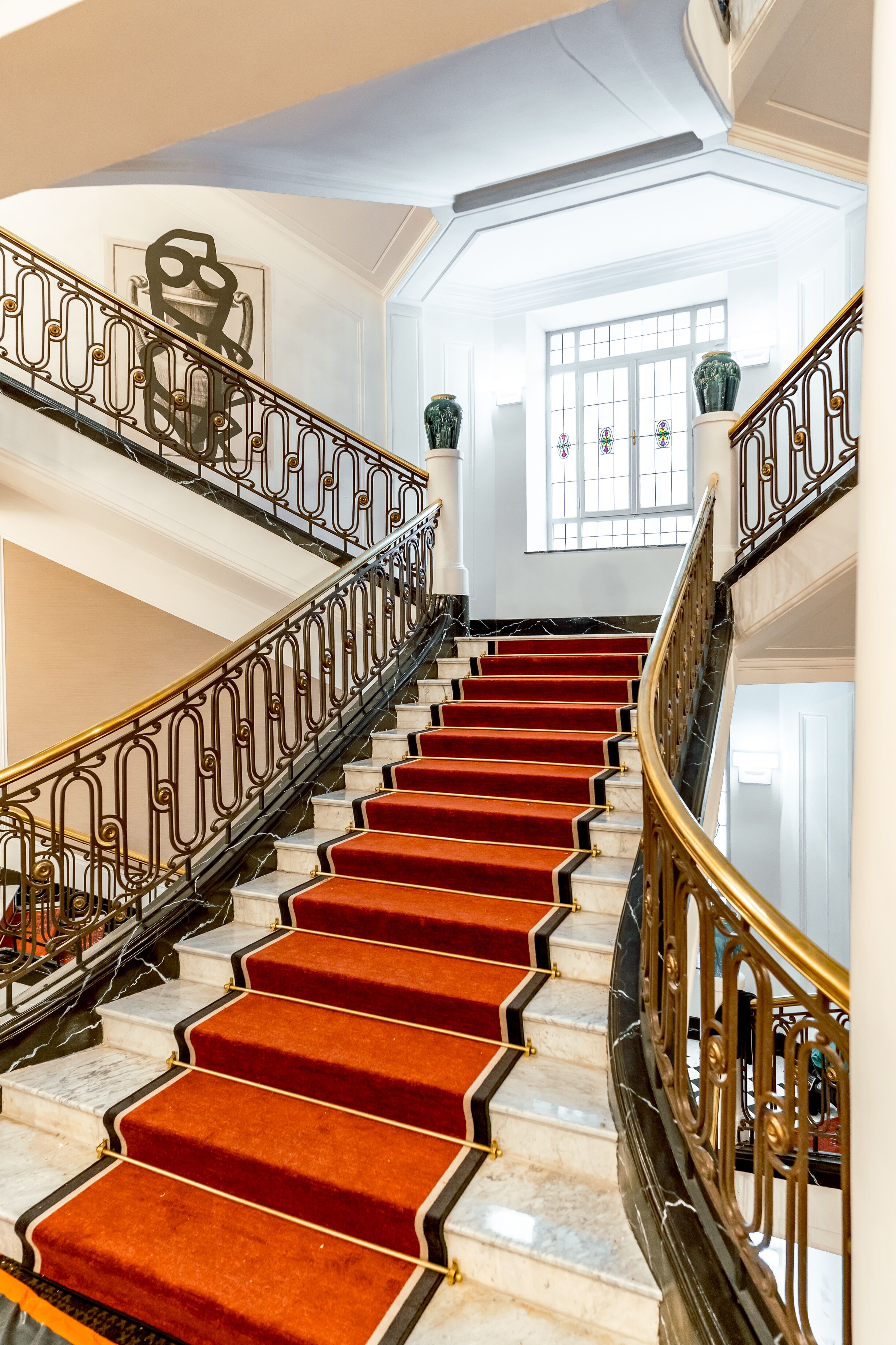 Una imponente escalera con peldaños alfombrados de rojo y barandales de metal ornamentados.