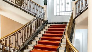 Una imponente escalera con peldaños alfombrados de rojo y barandales de metal ornamentados.