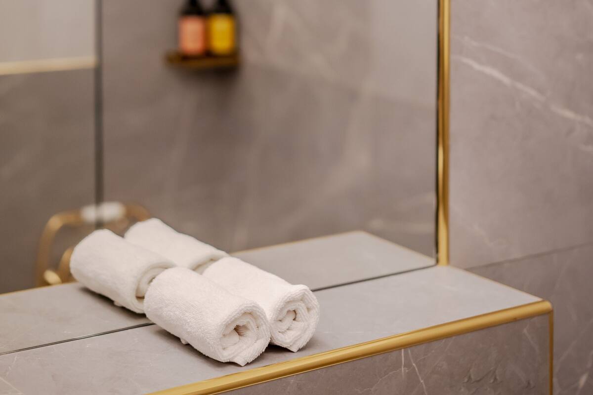A bathroom with a marble wall, a gold-framed mirror, and a towel on a white counter.