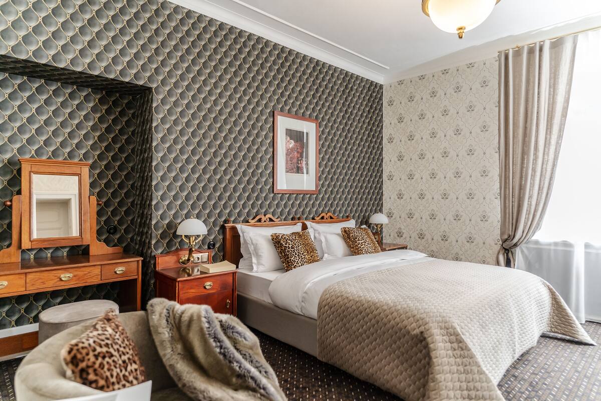 A hotel room with a large bed, a wooden nightstand, a mirror, and a patterned wall.