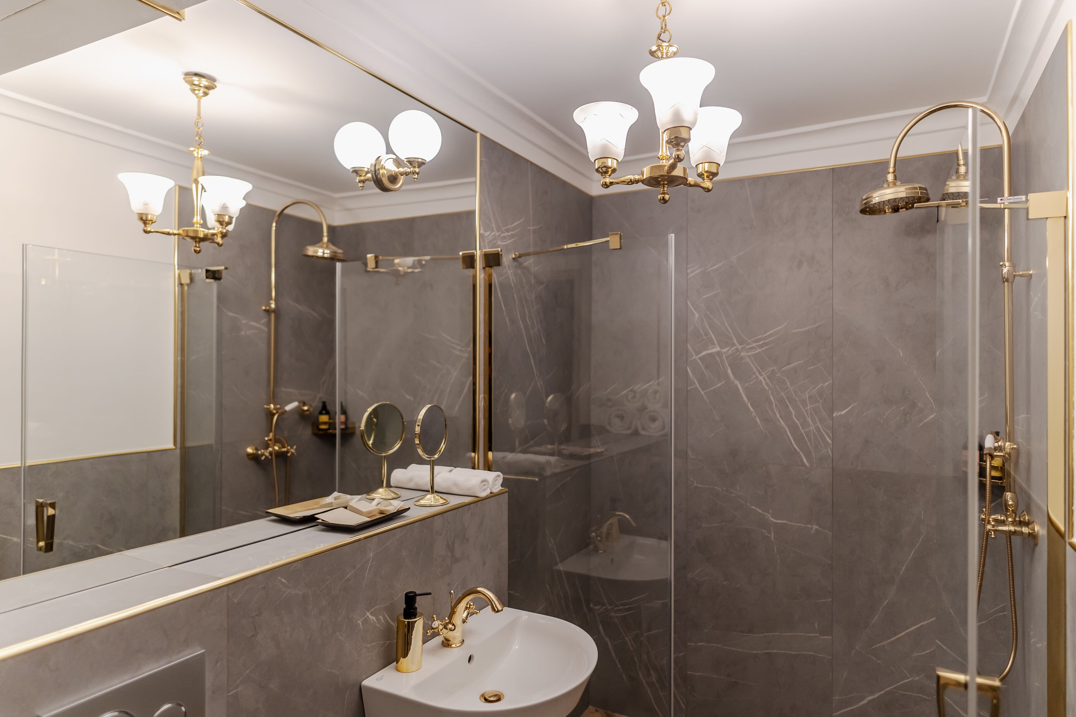A modern bathroom with a large mirror, gold fixtures, and a glass-enclosed shower.