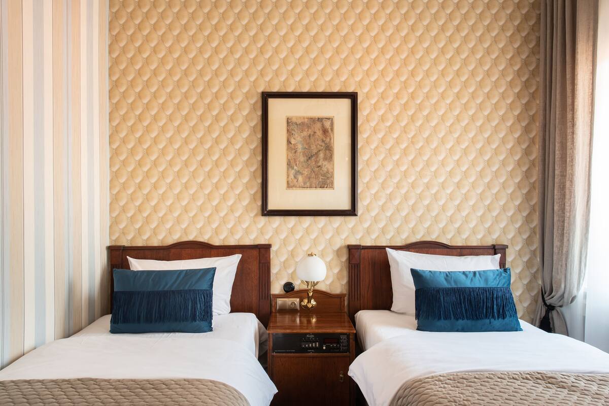 A hotel room with two beds, a framed picture on the wall, and a nightstand with a lamp.