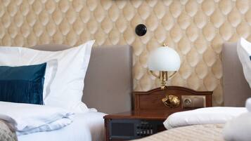 A hotel room with a quilted wall pattern, a bed with white bedding, a bedside table with a lamp, and a framed picture above the bed.