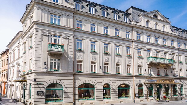 Un edificio histórico de varios pisos, con amplias ventanas y balcones adornados con macetas de flores.