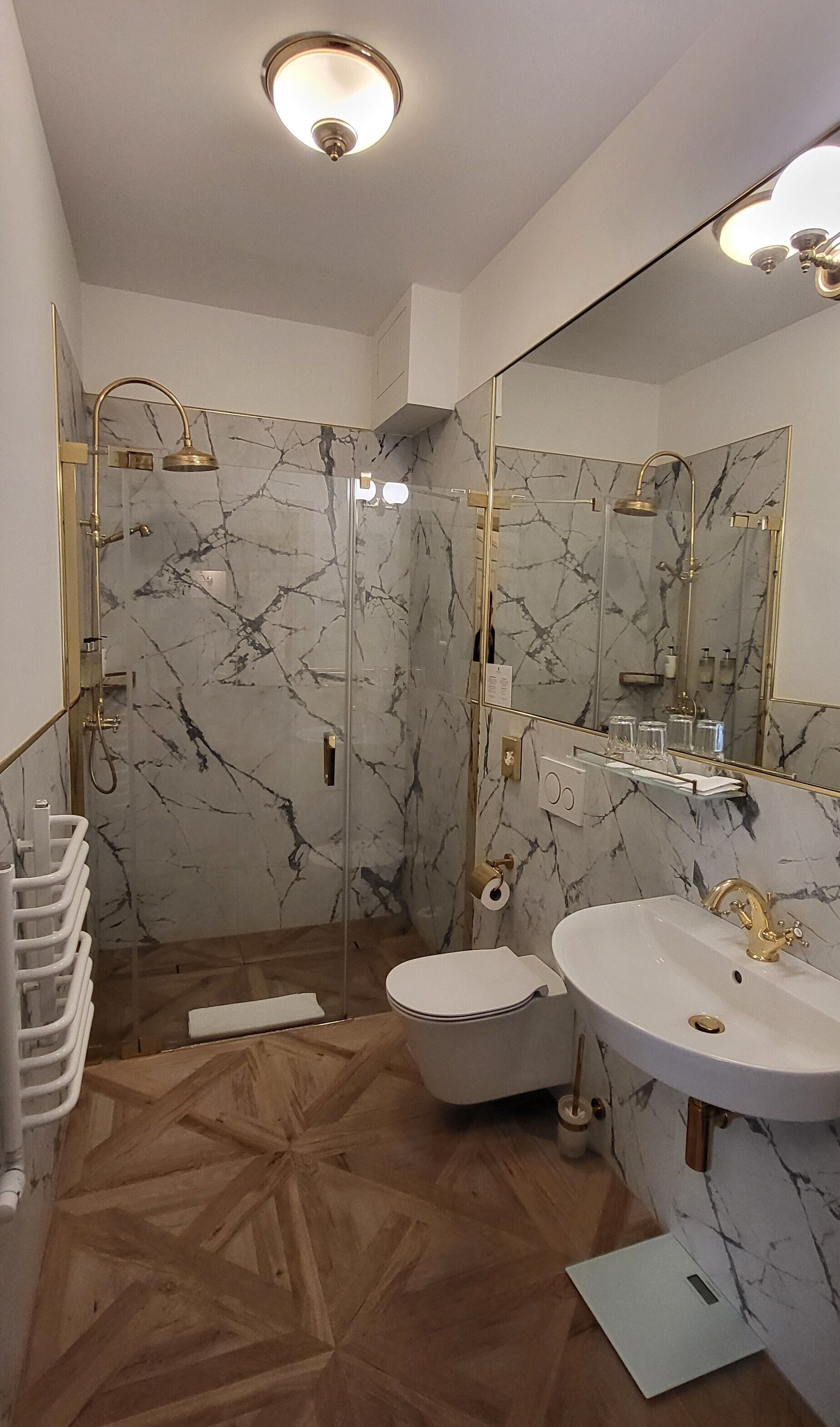A modern bathroom with a marble shower wall, a freestanding bathtub, and a large mirror.