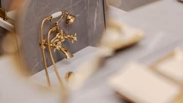 A bathroom with a marble wall, a gold faucet, and a white sink.