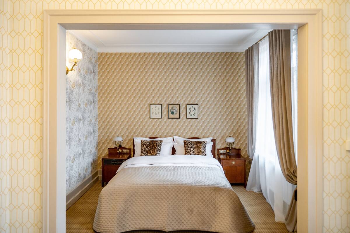 A hotel room with a bed, nightstands, and a wall with patterned wallpaper.