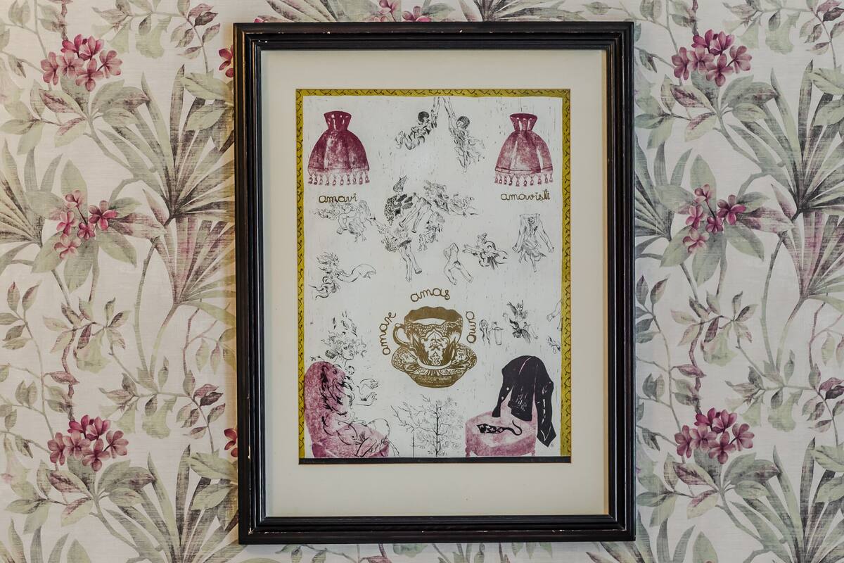 A framed artwork on a wall with floral wallpaper, a bed with brown and white pillows, and a wooden headboard.