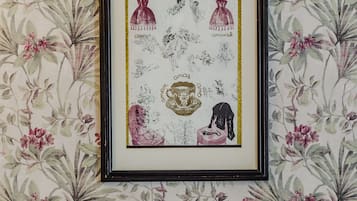 Une œuvre d’art encadrée accrochée au mur, qui est recouvert d’un papier peint à motifs floraux, un lit avec des oreillers marron et blancs, et une tête de lit en bois.