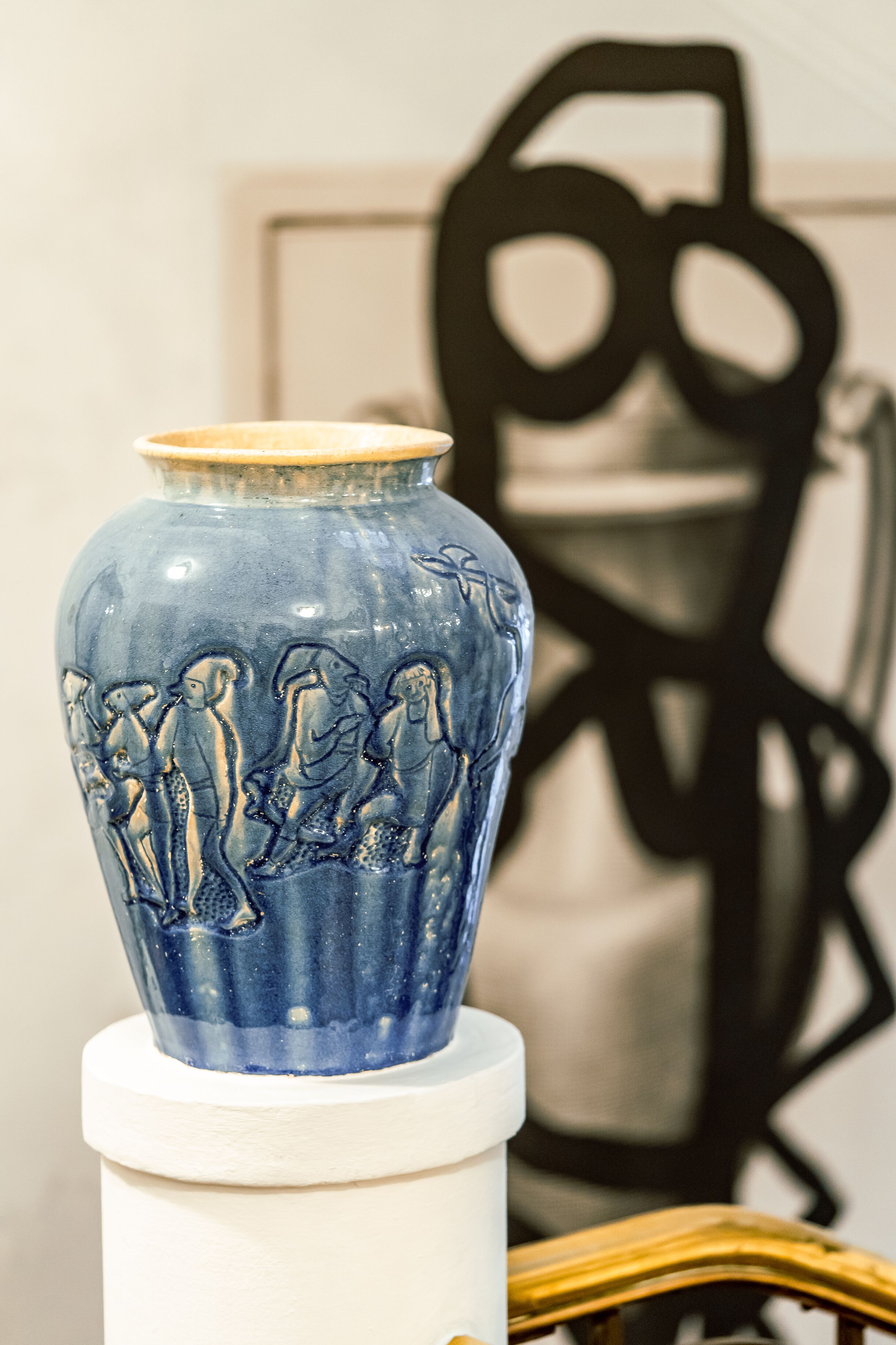A blue ceramic vase with a white base, placed on a white pedestal.