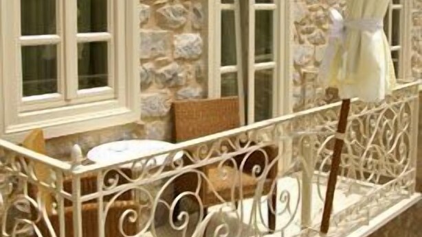 A stone building with a balcony featuring a wrought iron railing and a white umbrella. - Angelica Boutique Hotel (Hydra)