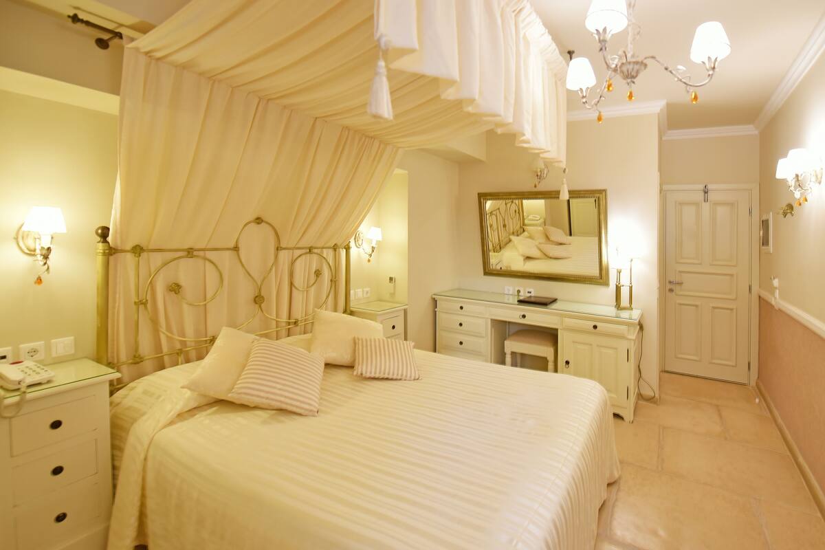 A bedroom with a canopy bed, a vanity with a mirror, and a door.