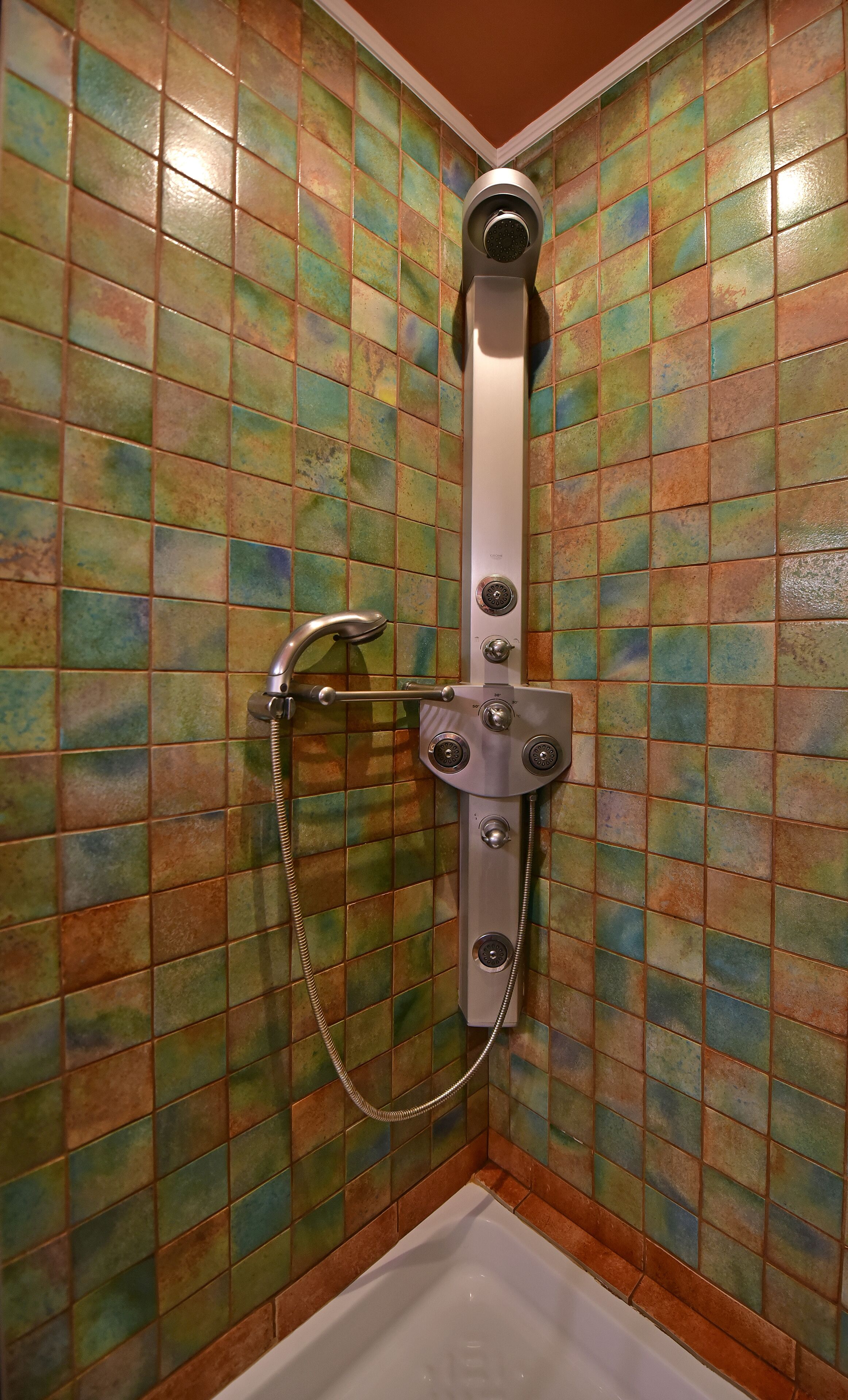 Ducha con cabezal de ducha manual y manguera, montada en una pared con azulejos multicolores.