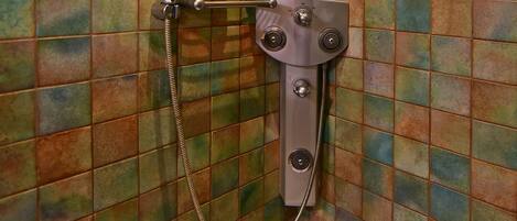 Ducha con cabezal de ducha manual y manguera, montada en una pared con azulejos multicolores.
