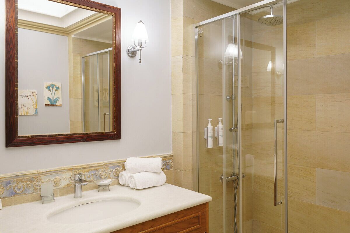 Un baño con un espejo grande, un lavabo, cabina de ducha de vidrio y detalles decorativos en la pared.