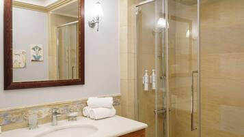 Un baño con un espejo grande, un lavabo, cabina de ducha de vidrio y detalles decorativos en la pared.