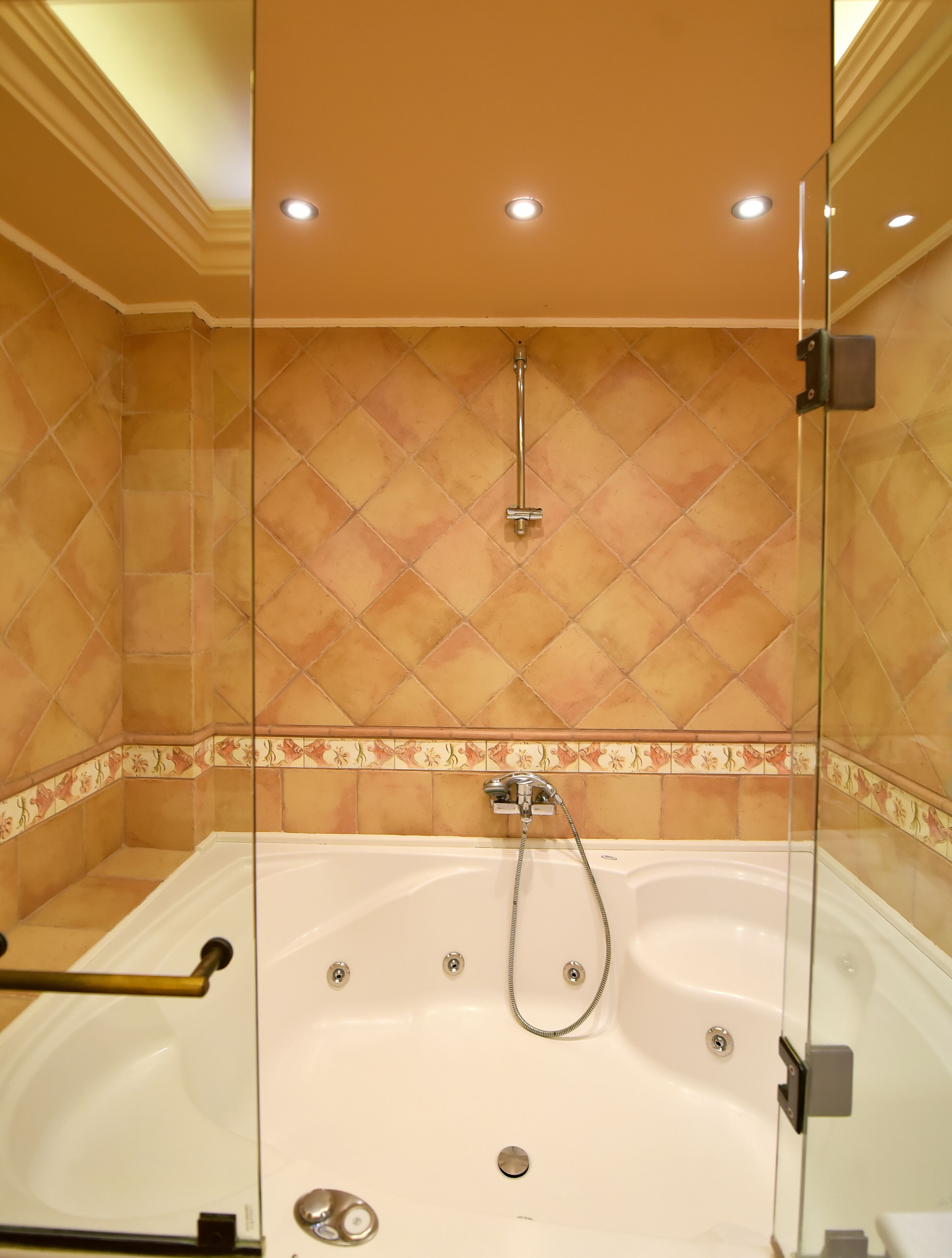 Una ducha a pie con cerramiento de vidrio, una bañera independiente, paredes con azulejos e iluminación empotrada en el techo.