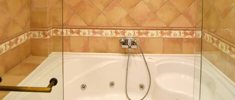 Una ducha a pie con cerramiento de vidrio, una bañera independiente, paredes con azulejos e iluminación empotrada en el techo.