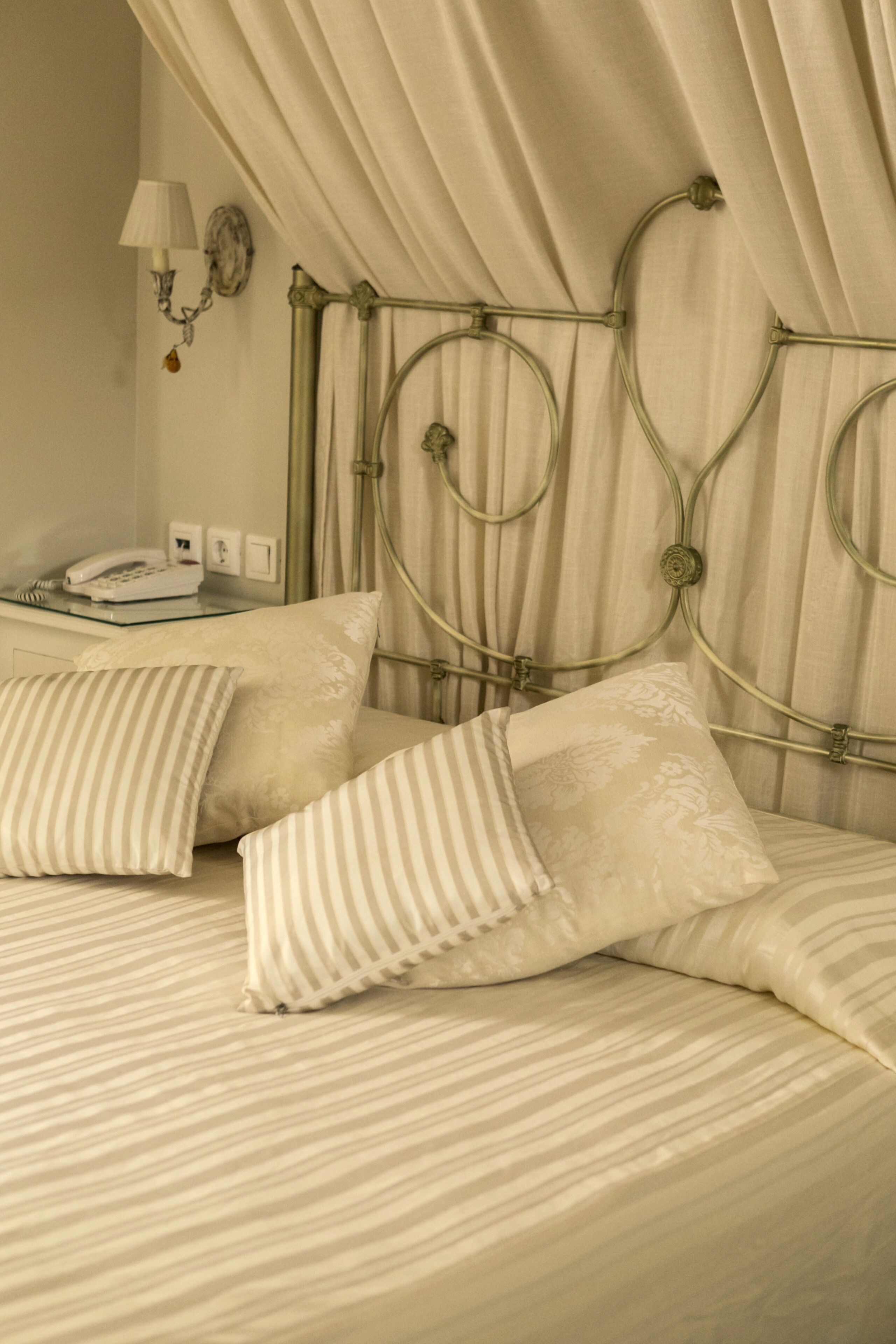 A bed with a metal headboard, two pillows, a bedside table with a lamp, and a telephone.