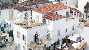 A white building with a red-tiled roof, multiple balconies, and outdoor seating areas.