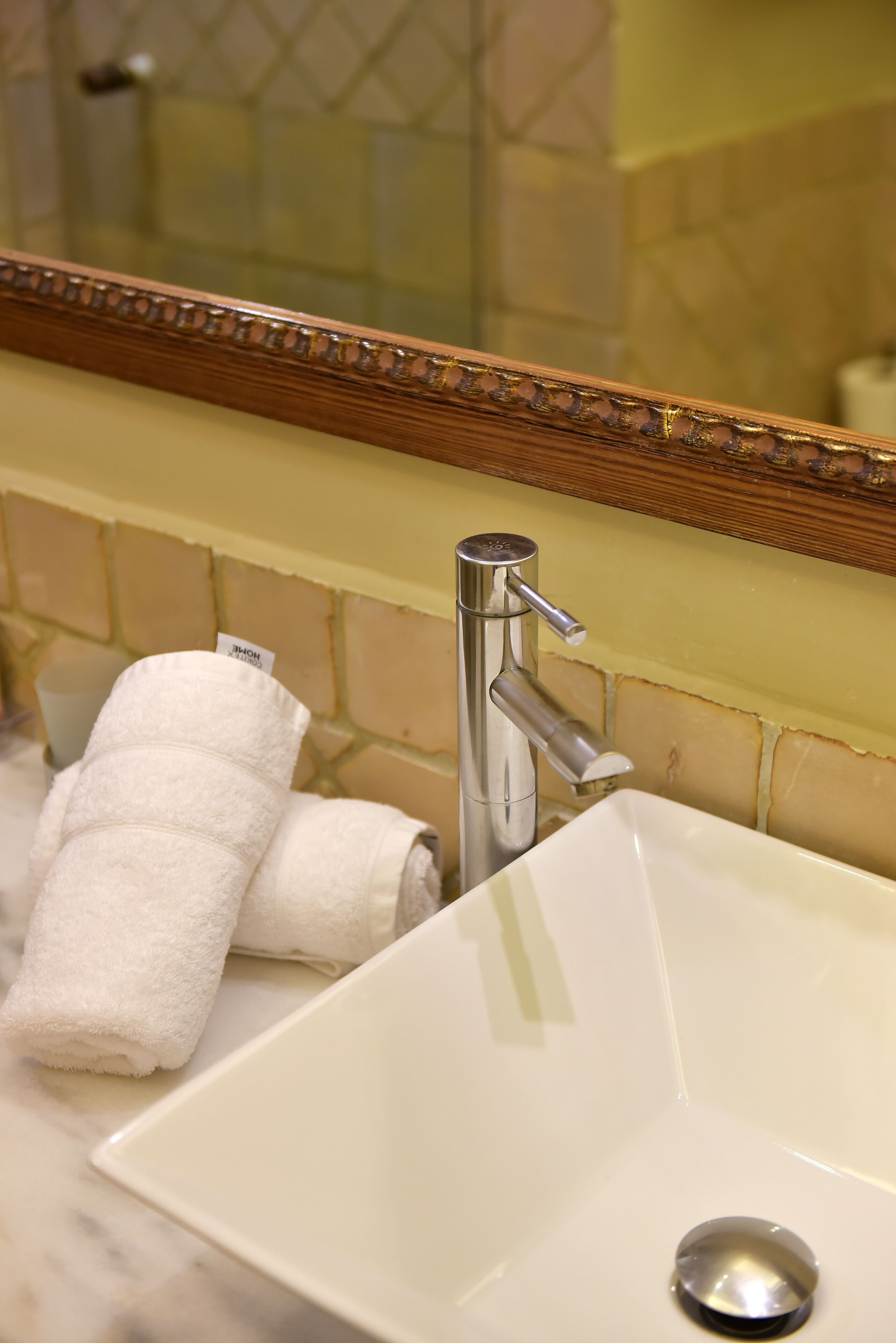 A bathroom with a white sink, a mirror with a wooden frame, and a towel rack with white towels.