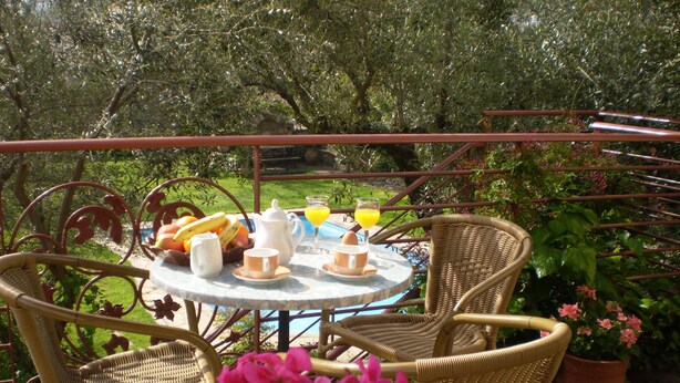 Une table ronde entourée de chaises en osier, une plante en pot et une table dressée pour le petit-déjeuner avec des œufs, des toasts et du jus de fruits.