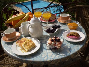 Una mesa dispuesta para el desayuno con frutas, pan y bebidas, con vista a una piscina.