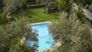 Une piscine rectangulaire entourée d’une végétation luxuriante et de murs en pierre.