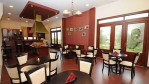 Un espace repas avec des tables et des chaises rondes, une cuisine à l’arrière-plan et de grandes fenêtres offrant une vue dégagée.