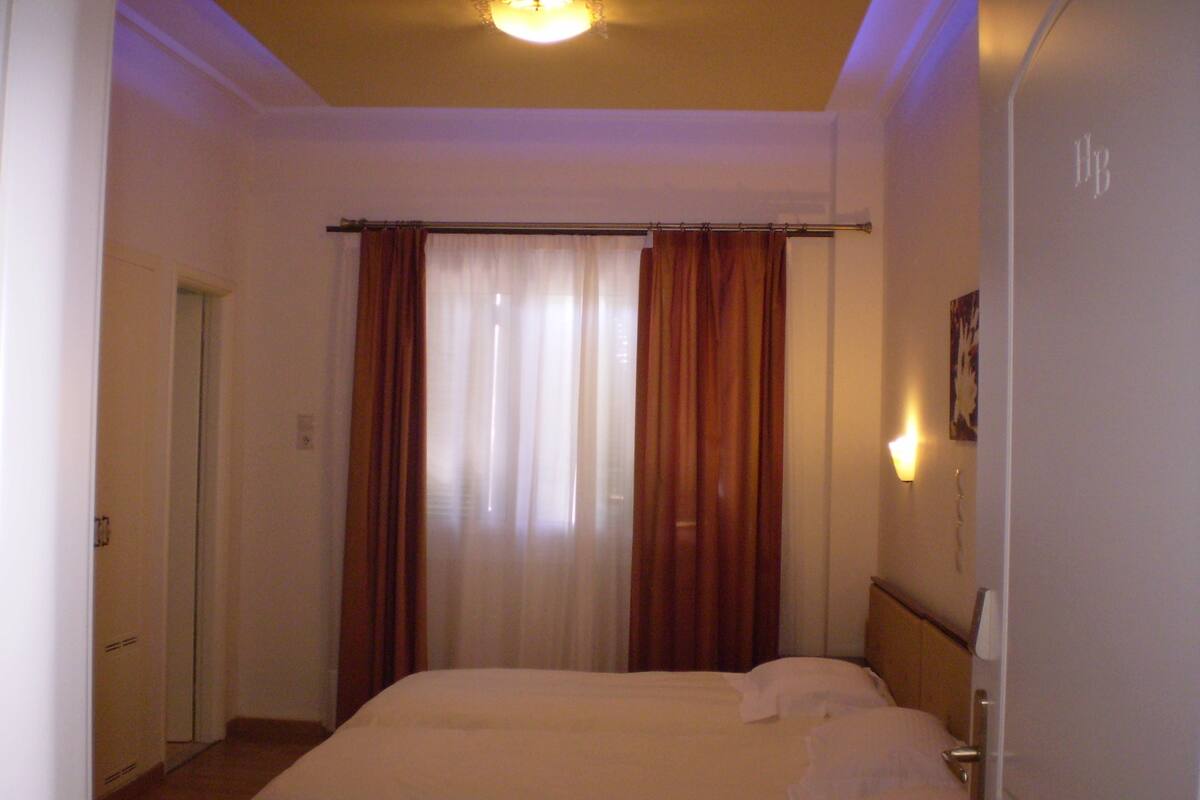 A hotel room with a bed, curtains, a door, and a light fixture.