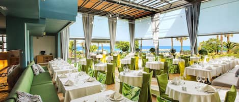 Un restaurante con varias mesas y sillas, un sofá verde y vista al océano.