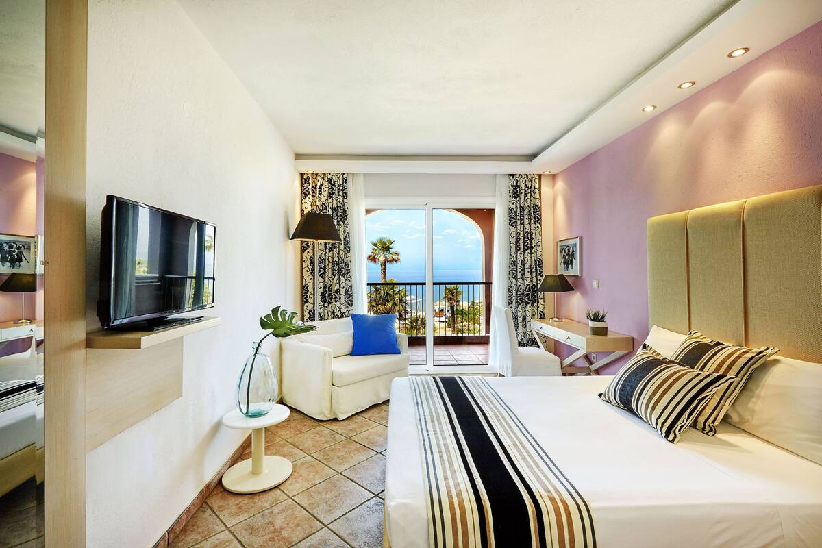 Une chambre d’hôtel avec un lit, une télévision, un canapé et un balcon donnant sur la mer.